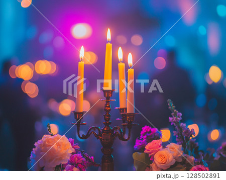 A close-up of a candelabra with lit white candles next to a bouquet of pink and white flowers, all set against a blurry purple background with bokeh lights. 128502891