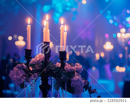 A close-up of a candelabra with lit white candles next to a bouquet of pink and white flowers, all set against a blurry purple background with bokeh lights. 128502911