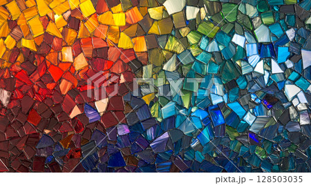 A vibrant mosaic made of irregular, colorful glass pieces, transitioning from warm reds and yellows on the left to cool blues and greens on the right. 128503035