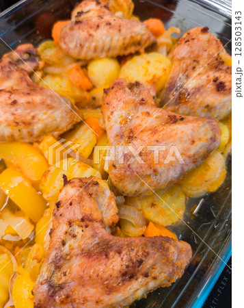 Delicious roasted chicken wings with potatoes, carrots, and onions baking in glass tray 128503143