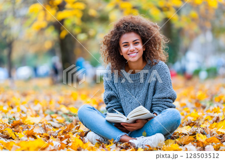 Smiling teenage girl with books in autumn park 128503512