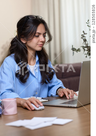 portrait of woman in blue shirt working using laptop in home office 128503816
