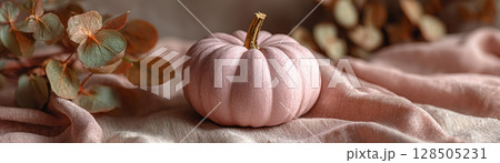 A soft blush toned pumpkin on a linen tablecloth with delicate floral accents 128505231