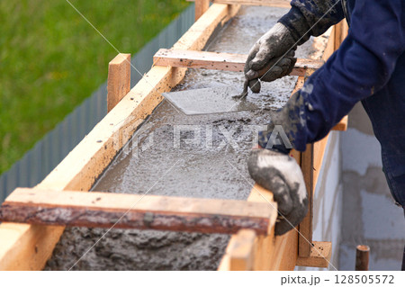 Worker levels concrete in formwork using a trowel Worker levels concrete in formwork using a trowel 128505572