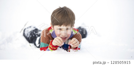A funny little boy in colorful clothes lies in the snow. A hardened child in winter. A funny little boy in colorful clothes lies in the snow. A hardened child in winter. 128505915