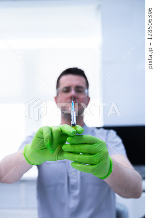 Healthcare Professional Holding a Syringe in a Medical Setting, Preparing for a Vaccination Procedure with Emphasis on Sterile Practices and Patient Care Principles Healthcare Professional Holding a Syringe in a Medical Setting, Preparing for a Vaccination Procedure with Emphasis on Sterile Practices and Patient Care Principles 128506396
