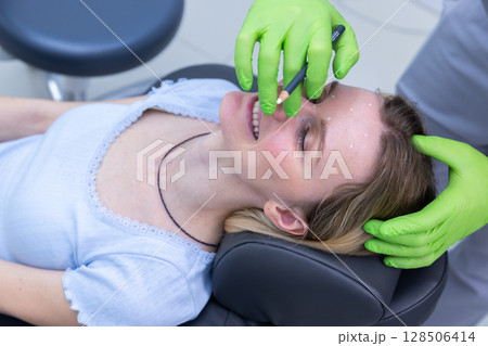 A Close-Up of a Beauty Procedure: A Woman Smiling While Receiving Cosmetic Treatment with a Professional Marking Her Forehead in a Modern Clinic Setting A Close-Up of a Beauty Procedure: A Woman Smiling While Receiving Cosmetic Treatment with a Professional Marking Her Forehead in a Modern Clinic Setting 128506414