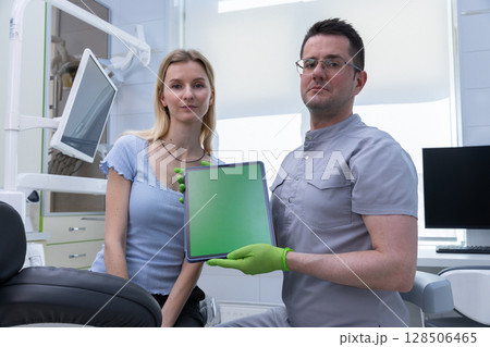 A confident dentist showcasing a digital tablet in a modern dental office alongside a patient, highlighting the use of technology in oral health care practices. A confident dentist showcasing a digital tablet in a modern dental office alongside a patient, highlighting the use of technology in oral health care practices. 128506465