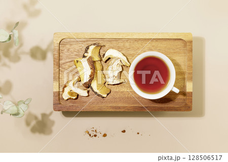 Mushroom tea. Cup of fresh mushroom tea and dry mushrooms on wooden small table on beige background with leaves. Healthy vegan or vegetarian food. New Superfood Trend. Flat lay 128506517
