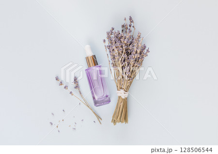 Wild-harvested beauty. Dropper bottle with natural lavender serum or cosmetic oil and lavender flowers on a blue background. Organic herbal cosmetics. Flat lay Wild-harvested beauty. Dropper bottle with natural lavender serum or cosmetic oil and lavender flowers on a blue background. Organic herbal cosmetics. Flat lay 128506544