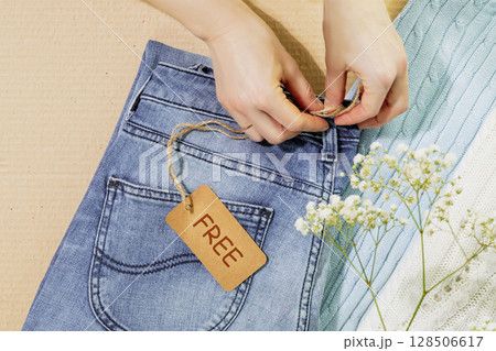 Sustainable life style with female hands holding label with text Free on clothes ready for a garage sale. Circular fashion, eco friendly sustainable shopping, thrifty shop and second hand concept 128506617