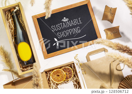 Eco friendly shopping. Craft cardboard gift boxes, wooden box with bottle of champagne and blackboard with text Sustainable Shopping on beige background. Zero Waste, plastic free, eco package concept Eco friendly shopping. Craft cardboard gift boxes, wooden box with bottle of champagne and blackboard with text Sustainable Shopping on beige background. Zero Waste, plastic free, eco package concept 128506712