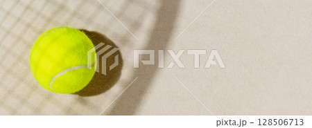 Tennis banner with tennis yellow ball on the sand beach with racket shadow. Tennis competitions, healthy sport and outdoor activities concept. Flat lay, banner size, copy space Tennis banner with tennis yellow ball on the sand beach with racket shadow. Tennis competitions, healthy sport and outdoor activities concept. Flat lay, banner size, copy space 128506713