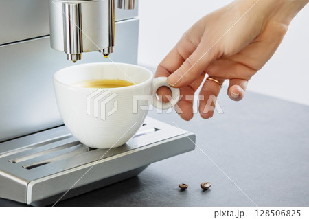 Female hand taking of cup of fresh hot espresso pouring from coffee machine. Professional coffee brewing. Cup of natural espresso. Coffee break. Good morning. Life style. Soft focus Female hand taking of cup of fresh hot espresso pouring from coffee machine. Professional coffee brewing. Cup of natural espresso. Coffee break. Good morning. Life style. Soft focus 128506825