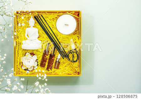 Holiday composition with recovering kit for meditation, yoga and relaxation. Yellow gift box with buddha statue, aroma sticks, natural oils, candle and crystals. Preparing healthy surprise. Copy space Holiday composition with recovering kit for meditation, yoga and relaxation. Yellow gift box with buddha statue, aroma sticks, natural oils, candle and crystals. Preparing healthy surprise. Copy space 128506875