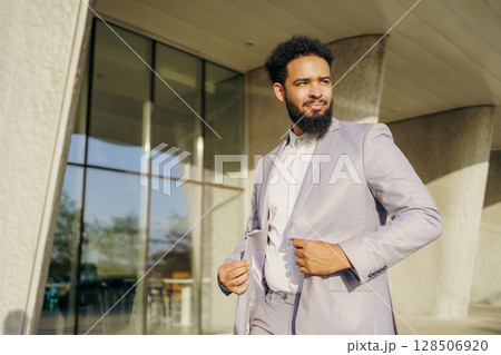 A stylish man in a sharp suit stands confidently by a modern building, embodying charm A stylish man in a sharp suit stands confidently by a modern building, embodying charm 128506920