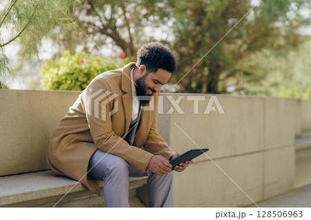 A man is using a tablet outdoors, enjoying a relaxed moment while being in natures beauty 128506963
