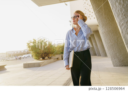 A Stylish Businesswoman is Confidently Walking Outdoors in a Vibrant and Dynamic City Setting A Stylish Businesswoman is Confidently Walking Outdoors in a Vibrant and Dynamic City Setting 128506964