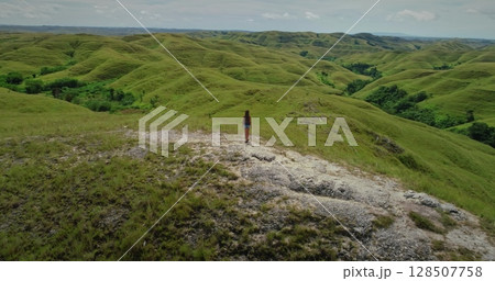 Female tourist admiring the idyllic rolling green hills landscape of Sumba Island in Indonesia, a popular travel destination for nature lovers 128507758