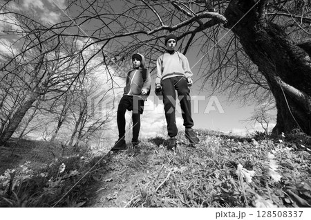 Two young people hiking on a trail, under a large tree. Black and white photography. 128508337