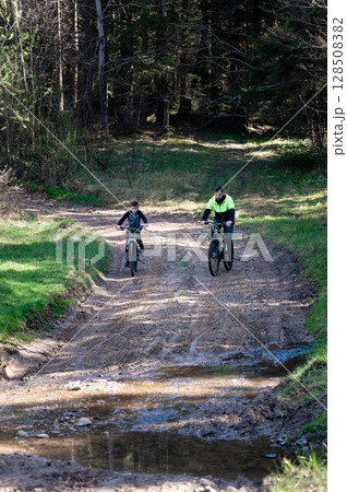 Father and son mountain biking on a forest trail, enjoying a sunny day outdoors. 128508382