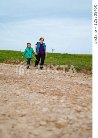 Grandmother and granddaughter holding hands, enjoying a leisurely stroll along a countryside path. 128508450