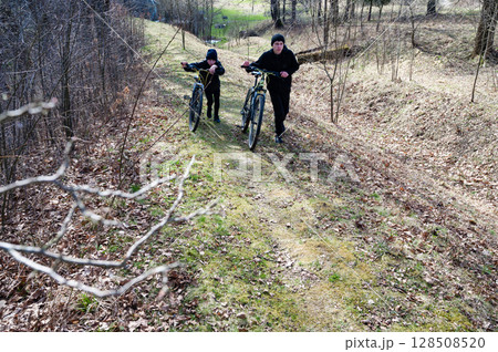 Two boys walk their bikes along a wooded path, enjoying a spring day outdoors. Two boys walk their bikes along a wooded path, enjoying a spring day outdoors. 128508520