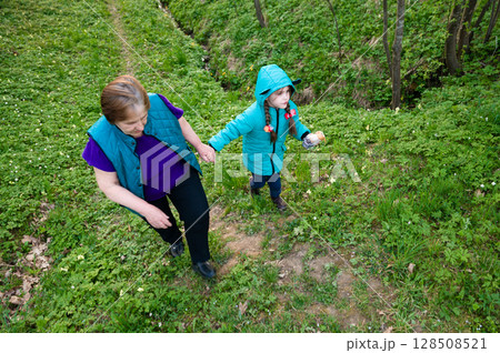 Grandmother and granddaughter enjoy a spring walk in the woods, holding hands. Grandmother and granddaughter enjoy a spring walk in the woods, holding hands. 128508521