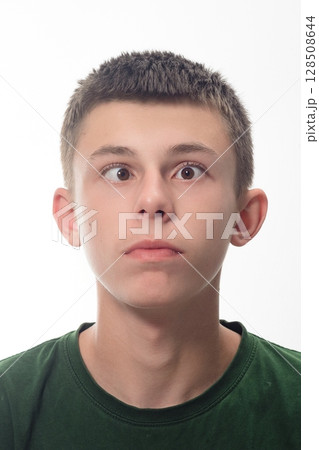 Teenage boy with eyes crossed, looking up. Close-up portrait against a white background. 128508644