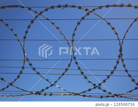 Flat security barrier made of reinforced barbed tape on the fence. 128508738