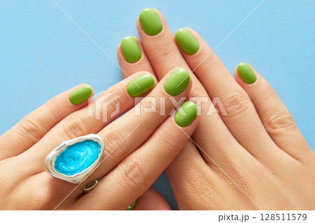 Womans hands with green manicure close up on blue background. Beauty treatment spa body care Womans hands with green manicure close up on blue background. Beauty treatment spa body care 128511579