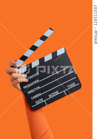Womans hand holding clapperboard on an orange background 128511587