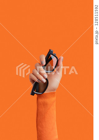 Womans hand holding 3d glasses on an orange background 128511592