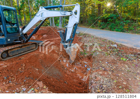 Heavy machinery digs into earth trench for installed drainage pipe Heavy machinery digs into earth trench for installed drainage pipe 128511804