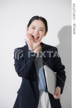 パソコン持って立つスーツを着たカメラ目線の若いかわいい女性のビジネスイメージ上半身 応援や声援 パソコン持って立つスーツを着たカメラ目線の若いかわいい女性のビジネスイメージ上半身 応援や声援 128512559