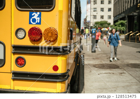Bright yellow school bus parked on city street features accessibility symbol. Urban environment showcases calm atmosphere under sunny sky, highlighting transportation accessibility. Bright yellow school bus parked on city street features accessibility symbol. Urban environment showcases calm atmosphere under sunny sky, highlighting transportation accessibility. 128513475