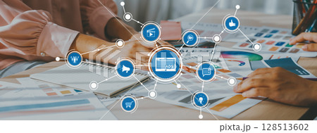 Hands Collaborating on Marketing Strategy with Graphs, Notebooks, and Digital Icons Depicting Advertising Concepts in Modern Office Setting. Amity 128513602
