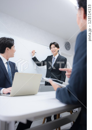 社内打ち合わせでプレゼンをするスーツを着たハンサムな男性ビジネスマン　ホワイトボードの前に立つ話す	 128514133