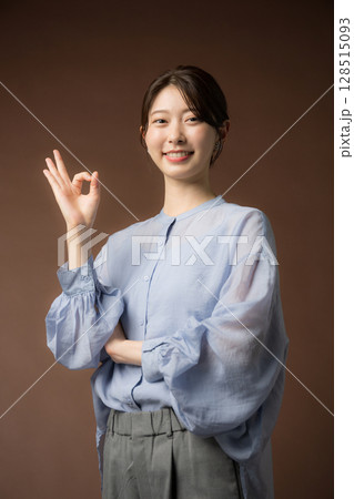 茶色い背景でビジネスシーンに使いやすい笑顔の女性　OKのポーズ	 128515093