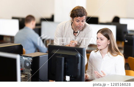 Adult male teacher helps woman work on computer 128516028