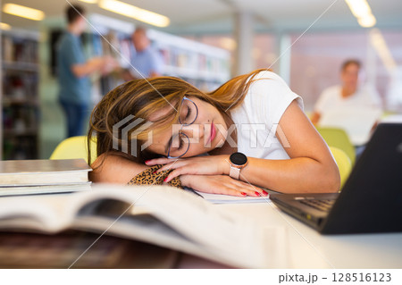 Tired female student fell asleep at the table in library 128516123
