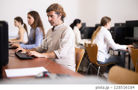 Man student of computer courses looks at monitor screen, types on keyboard and does work 128516184