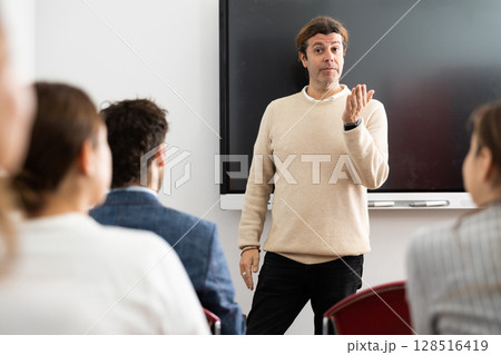 Confident male leader, trainer near interactive board talking to group of people, brainstorming, discussing ideas in auditory Confident male leader, trainer near interactive board talking to group of people, brainstorming, discussing ideas in auditory 128516419