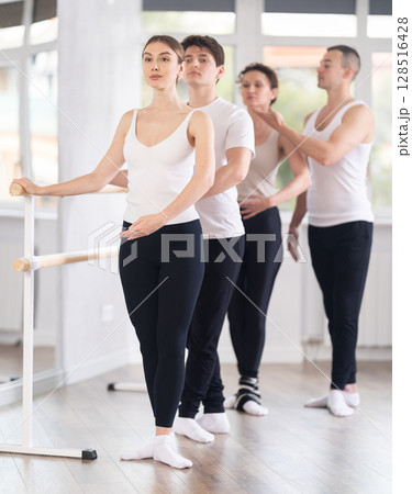Young man trainer corrects dancers at barre 128516428
