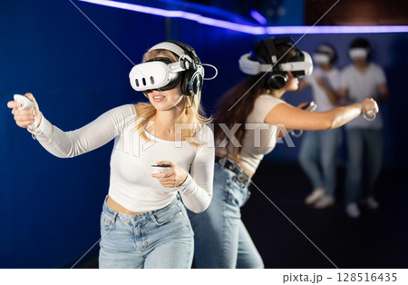 Two girls wearing virtual reality glasses participate in game with opponents Two girls wearing virtual reality glasses participate in game with opponents 128516435