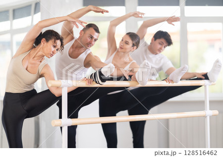 Group of dancers doing stretching at barre 128516462
