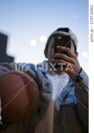 ブルーアワーの夕方にバスケットボールを持ってsns投稿や写真を撮る男の子 縦 ブルーアワーの夕方にバスケットボールを持ってsns投稿や写真を撮る男の子 縦 128516862