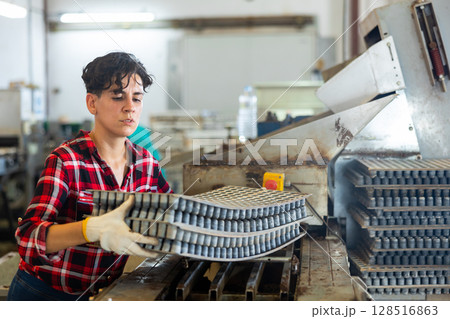 Attentive plantation female worker loading empty trays in automatic seed planting line preparing for planting seeds in greenhouse 128516863