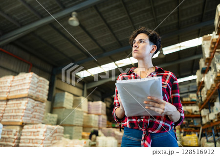 Female storekeeper checks availability of goods with documents in the building materials warehouse 128516912