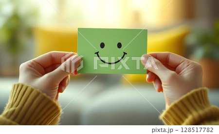 Individual displaying a smiley face paper, promoting mental health awareness and self-care in a supportive setting 128517782